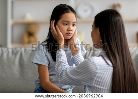 Childhood problems concept. Young mother comforting her sad offended daughter after quarrel at home. Asian woman calming down her child, sitting together in living room interior Royalty-Free Stock Photo #2036962904