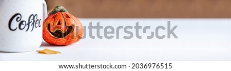 Banner of ceramic orange small smile halloween pumpkin with autumn leaves near it and coffee cup with text "coffee" on it. Halloween holiday concept with copy space on bright background
