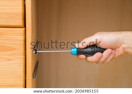 Young adult man hand using manual screwdriver and screwing screw in board of drawer for rail hinge. Assembling new wooden furniture. Closeup. Royalty-Free Stock Photo #2036985155