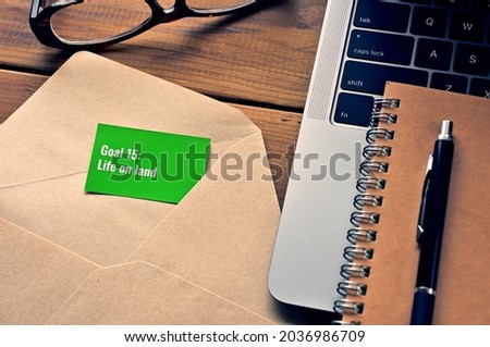 There is a card with the word of Goal 15:Life on land which is one of the goals of the Sustainable Development Goals.It's by the envelope or laptop computer.