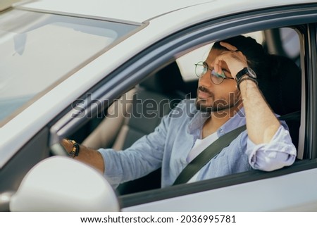 Thoughtful arab guy driving nice car, dreaming about something while stuck in traffic, pensive middle-eastern guy driver with fasten seat belt looking at road, leaning on his hand, copy space Royalty-Free Stock Photo #2036995781