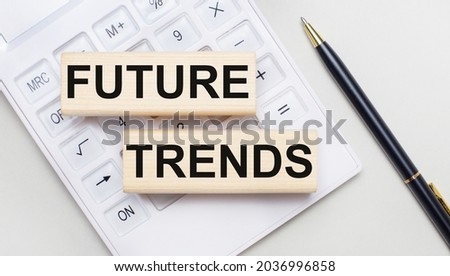 Wooden blocks with the text FUTURE TRENDS lie on a light background on a white calculator. Nearby is a black handle. Business concept