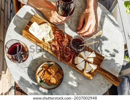 Varied appetizer Cheese board with soft cheese, fruit sauce and red wine on marble table for small party on summer sunny day Royalty-Free Stock Photo #2037002948