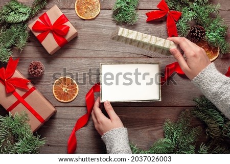 christmas gift background, hands open a christmas present on a wooden table with gift boxes and green spruce branches, empty gift, mock up for design, there is nothing in the gift box