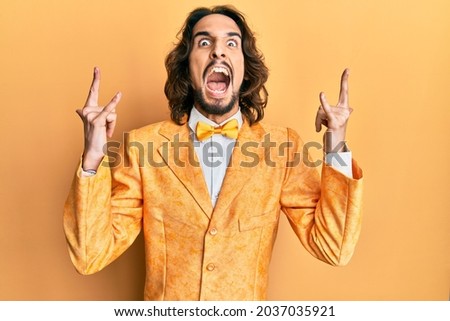 Young hispanic man wearing hipster elegant look shouting with crazy expression doing rock symbol with hands up. music star. heavy concept. 