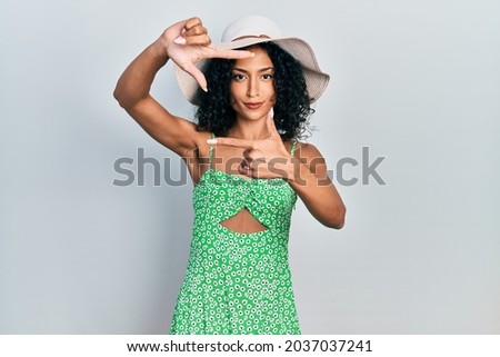 Young latin girl wearing summer hat smiling making frame with hands and fingers with happy face. creativity and photography concept. 