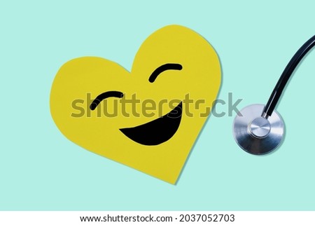 Yellow paper cut heart shape smiley face and cardiogram instrument on pastel green background.