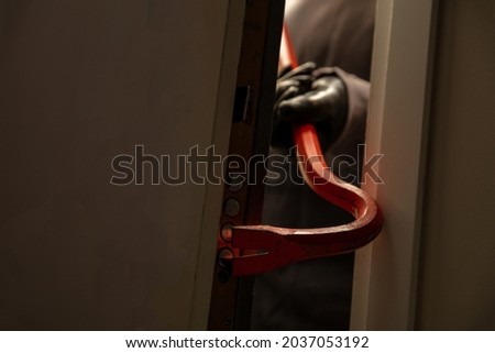 Burglar breaking a house aluminum door, for entering a house and stealing. Housebreak with crowbar. Red color metal crowbar closeup view Royalty-Free Stock Photo #2037053192