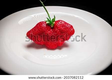  a strawberry with an original shape on a white plate
