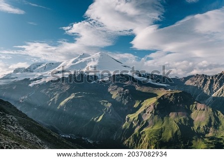 Majestic giant Elbrus at sunset on a warm summer cloudy evening, the sun's rays illuminate the valley