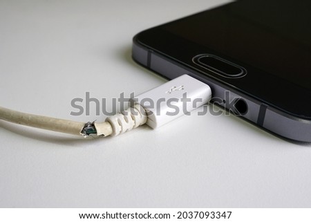 Old charger cable broken and smartphone, Defective charging cord, Connection deterioration device Royalty-Free Stock Photo #2037093347