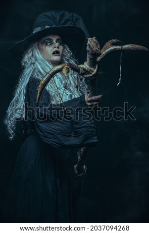 Halloween. Portrait of an ugly old witch standing with her magic staff on a black background . Witchcraft.