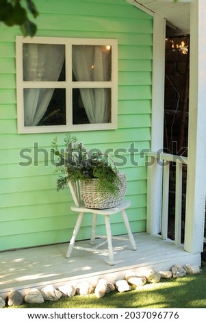 Cozy terrace with chair and basket with flowers. Decorations in summer patio for relax. Stylish fall decor on front porch home.  Exterior wooden porch home with garden furniture. Autumn porch home. 
