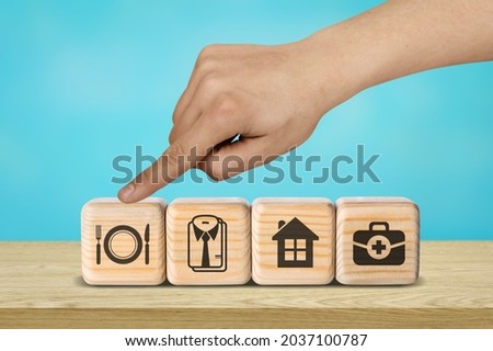 human hand placing cube with food, clothing, housing, medicine, needs concept.