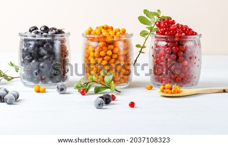 Three types of frozen bright wild berries in glass jars. Close-up, horizontal. Light background.