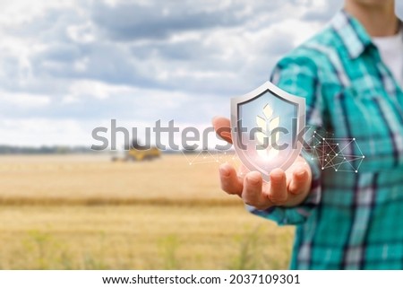 Harvest protection concept by farmers. Farmer shows a shield with an ear on the background of an agricultural field. Royalty-Free Stock Photo #2037109301