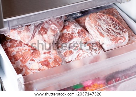 Meat in refrigerator freezer background. Closeup pork, meat and chicken leg in freezing compartment. Frozen food