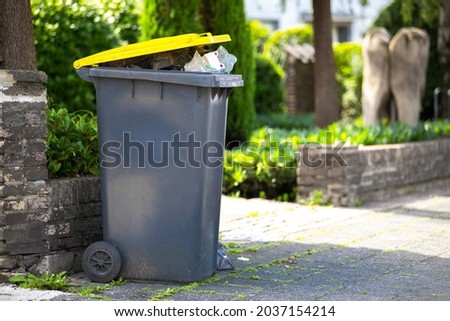 full garbage trash can standing at sidewalk next to street waiting to get collected and empty the recyclable plastic dump out of the black yellow container Royalty-Free Stock Photo #2037154214