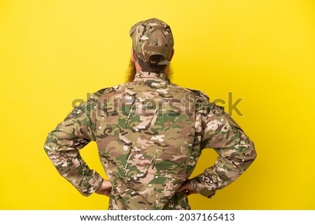 Military Redhead man over isolated on yellow background in back position