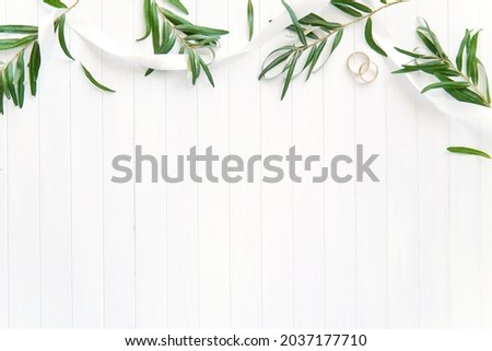 Wedding flat lay composition with green branches, white ribbon, golden rings, background with empty space for text or design.
