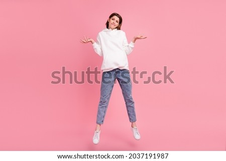 Full length photo of millennial lady jump shrug shoulders wear hoodie jeans sneakers isolated on pink background