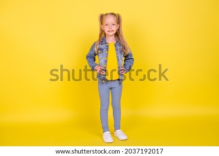 Full size photo of young little girl happy positive smile hands on waist confident celever isolated over yellow color background