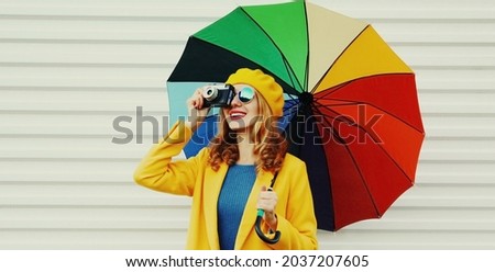 Autumn portrait of happy cheerful smiling young woman photographer with colorful umbrella and camera wearing a yellow coat and beret on a white background