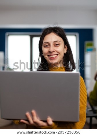 Woman designer creator looking at camera smiling while working in design post production agency. Videographer graphic editor standing in multimedia company holding laptop editing creative video
