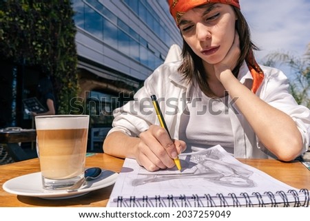 Portrait of a beautiful young woman sitting drinking coffee and drawing. Concept of joy, tranquility and relax.