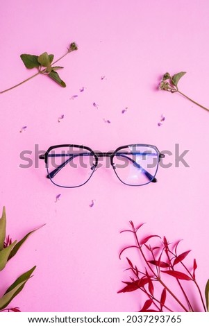 metal square glasses in the photo in minimal summer style on a pastel pink background. red leaf, green leaf, flower
