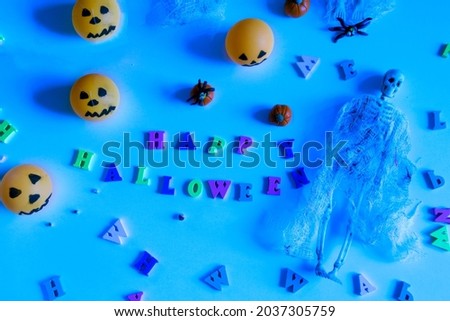 Halloween concept with pumpkins, skeleton, toy spiders and happy halloween lettering on blue background