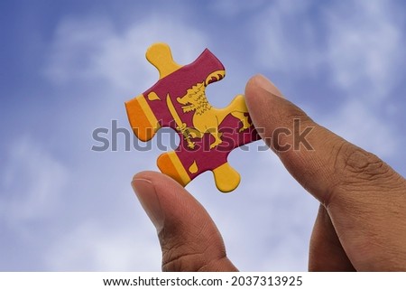 Hand holding piece of jigsaw puzzle with flag of Sri Lanka. Jigsaw puzzle of Sri Lanka flag on sky background.