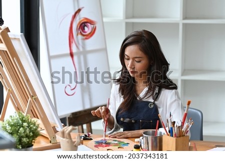 Beautiful female artist holding brush and mixing color oil painting on palette.