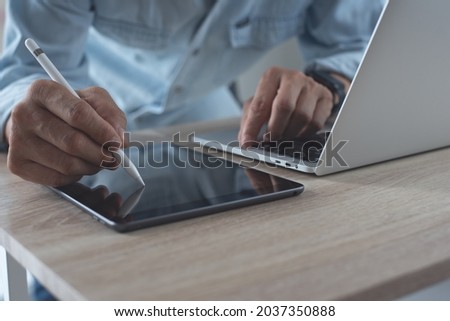 Close up of business man using electronic pen or stylus pencil signing e-document on digital tablet, online working on laptop computer at workplace, E-signing, online release, telework concept