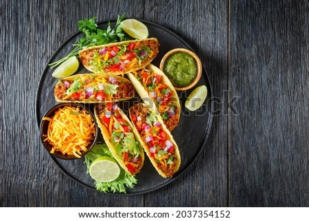 Ground Beef Tacos with shredded cheese, green salsa verde sauce, fresh lettuce, tomato, onion on a black platter with lime wedges, flat lay, free space