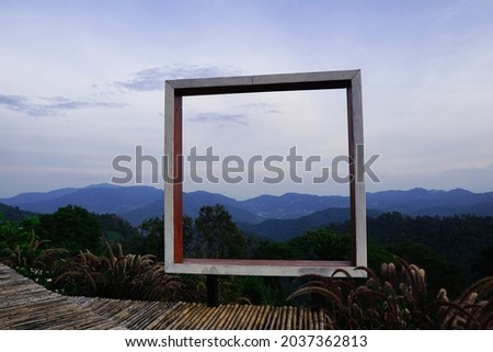 Take a photo with a square wooden frame and see the view. The old bamboo walkway is in the countryside with no terraces to prevent accidents on the background of forests and mountains.