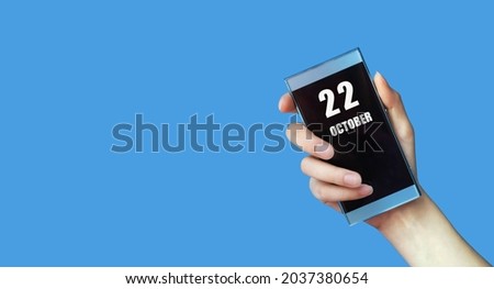 october 22. 22th day of the month, calendar date.Woman's hand holds mobile phone with blank screen on blue isolated background. Autumn month, day of the year concept.