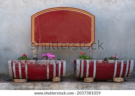 Red Wooden Signboard and Frame in a Garden and two Small Wooden Vases with Flowers.