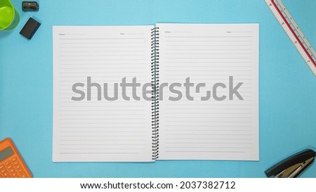Office table desk with set of colorful supplies, blue blank note pad, cup, pen, pc, crumpled paper, flower on blue background. Top view and copy space for text.
