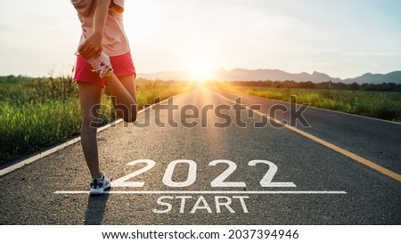 New year 2022 or start straight concept.word 2022 written on the asphalt road and athlete woman runner stretching leg preparing for new year at sunset.Concept of challenge or career path and change. Royalty-Free Stock Photo #2037394946