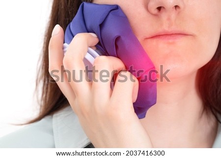 The girl attaches a medical bag with cold to the cheek of an aching tooth. Concept for pain relief and inflammation in dentistry with the help of cold, close-up Royalty-Free Stock Photo #2037416300