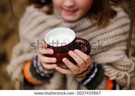 Cozy teenager girl with a cup of cocoa in the fall on the playground in the park, the child warms up with cocoa in the autumn day