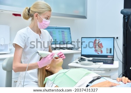 Orthodontist scaning patient with dental intraoral scanner and controls process on laptop screen. Prosthodontics and stomatology concept. Royalty-Free Stock Photo #2037431327