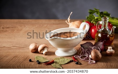 Gravy boat or pitcher with savory spicy gravy and fresh healthy assortment of vegetables, seasoning and olive oil on a wooden kitchen table with copyspace Royalty-Free Stock Photo #2037434870