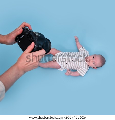 A photographer takes pictures of a newborn baby with a camera on a blue studio background. Photo session of children in the studio