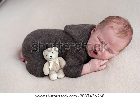 photography of a newborn boy. newborn baby in a brown suit with a soft toy. baby sleeps sweetly with a little teddy bear. plump cheeks of a boy