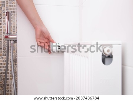 the woman turns on the heating radiator in the bathroom with a thermostat. Setting a comfortable temperature in the bathroom Royalty-Free Stock Photo #2037436784