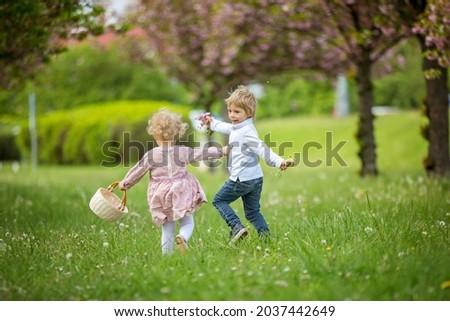 Beautiful children, toddler boy and girl, playing together in cherry blossom garden, running together and smiling with joy. Kids friendship, happy childhood