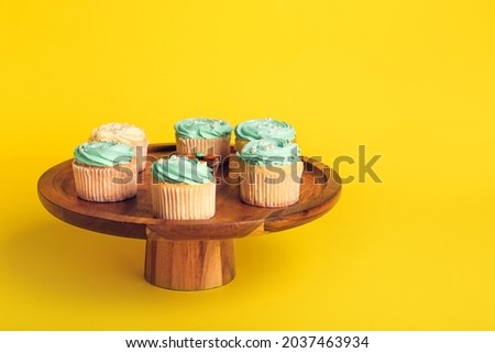 Dessert stand with tasty cupcakes on color background