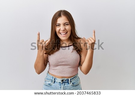 Young brunette woman standing over isolated background shouting with crazy expression doing rock symbol with hands up. music star. heavy concept. 